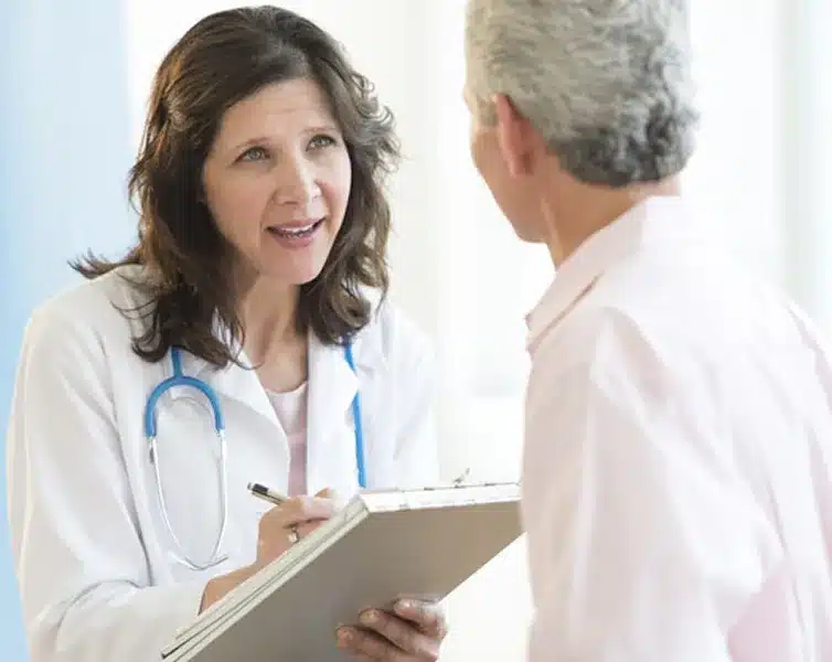 Home 7 Stem Cells Una doctora con bata blanca sonríe mientras habla con una paciente feliz sentada en la camilla, generando un ambiente de confianza durante la consulta médica.