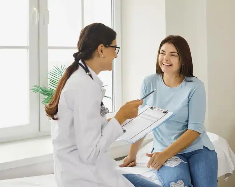 Home 10 Stem Cells Doctora con estetoscopio tomando notas en un portapapeles mientras conversa con un paciente mayor durante una consulta médica.