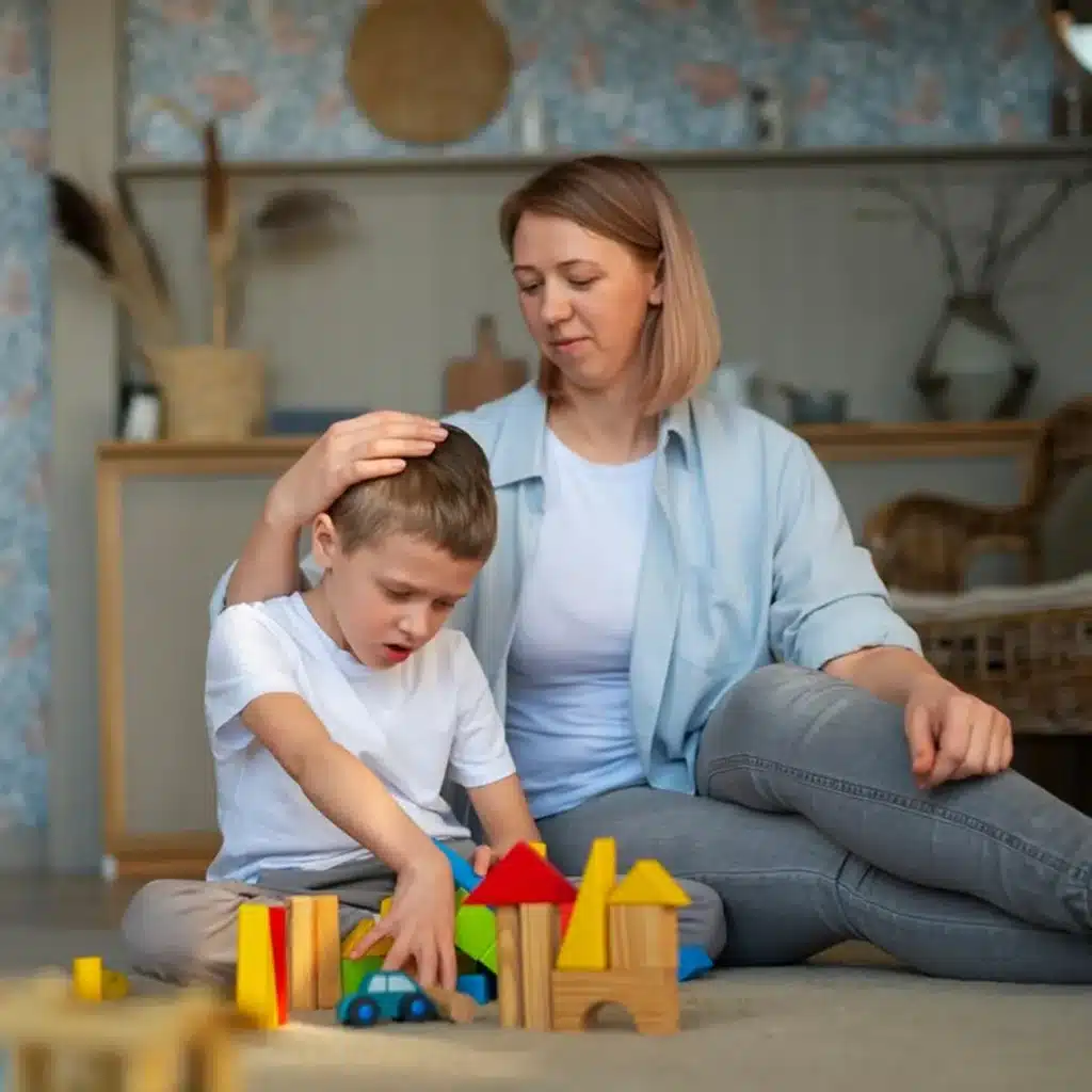 Madre acaricia a su hijo mientras él juega con bloques de construcción de madera en el suelo.