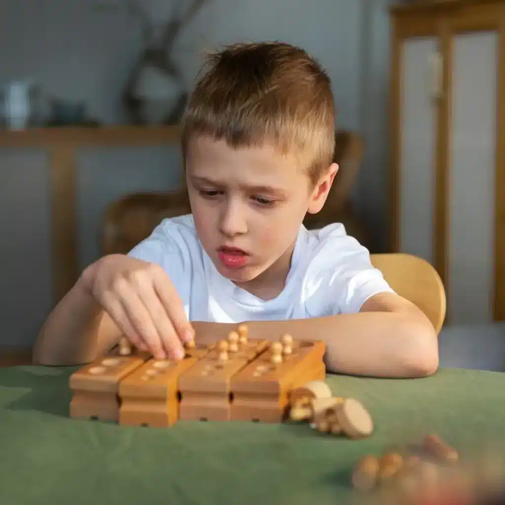 Niño de cabello rubio, concentrado y con expresión de pensar, jugando un juego de lógica o estrategia de mesa de madera con clavijas.